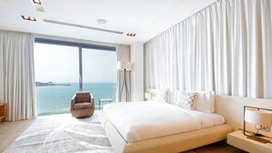 Een moderne hotelkamer met een groot bed, uitzicht op zee en een staande lamp.