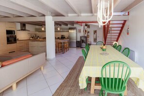 Une salle à manger spacieuse avec une longue table, des chaises vertes et une nappe à carreaux jaunes.