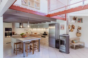 Une cuisine moderne dotée d’un îlot central, d’appareils électroménagers en acier inoxydable et d’un poêle à bois encastré.