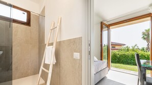 Une salle de bain moderne dotée d’une douche à parois de verre, d’une échelle en bois et d’une grande porte coulissante en verre donnant sur une chambre à coucher avec un lit et un coin repas.