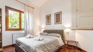 Un dormitorio con una cama, una ventana con cortinas, un radiador y dos cuadros en la pared.