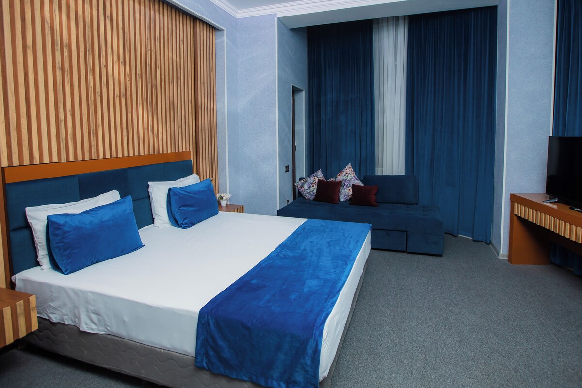 Una habitación de hotel moderna con una cama grande, un sofá, un televisor y una pared de acento de madera.