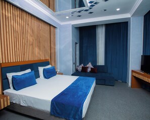 A modern hotel room with a large bed, a sofa, a TV, and a wooden accent wall. - Corniche White City Hotel (Baku)