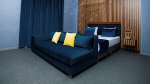 Een moderne hotelkamer met een donkerblauwe bank, een houten hoofdbord en een telefoon op een houten bijzettafeltje.