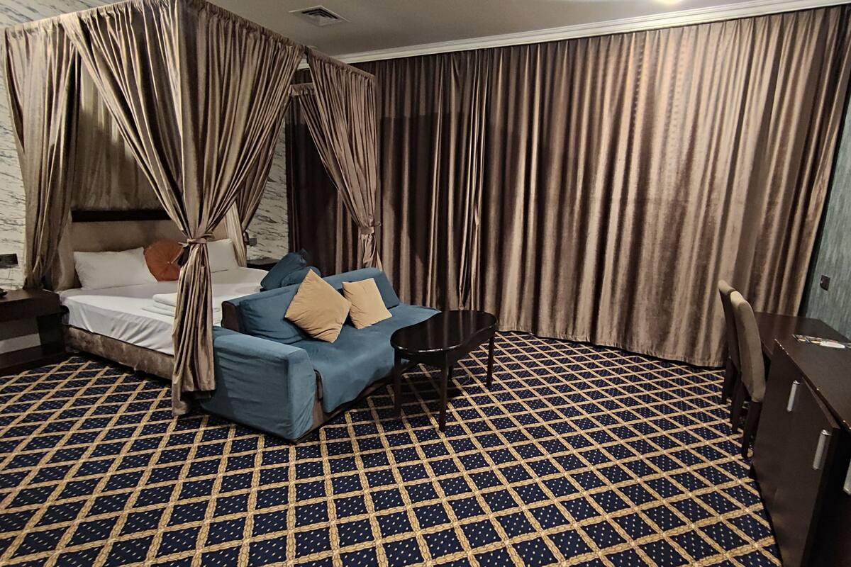 Una habitación de hotel con una cama, un sofá azul, una mesita y un televisor.
