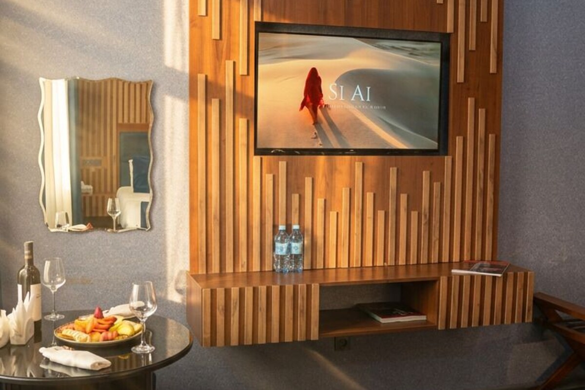 Una sala moderna con un televisor de pantalla plana montado en una pared de paneles de madera, un área de comedor con una mesa redonda y sillas, y un sofá azul.