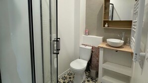 Un baño moderno con cabina de ducha de vidrio, inodoro, lavamanos y espejo.