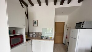 Cocina compacta con armarios blancos, un microondas rojo, una cafetera blanca y un refrigerador blanco.