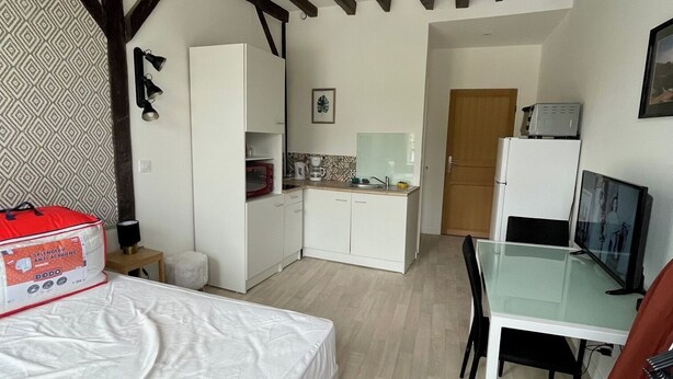 Una habitación compacta con cama, una kitchenette pequeña, una zona de comedor con mesa y sillas, y un televisor.