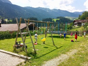 Un terrain de jeux avec des balançoires et une structure d’escalade, entouré d’une pelouse et avec des maisons en arrière-plan.