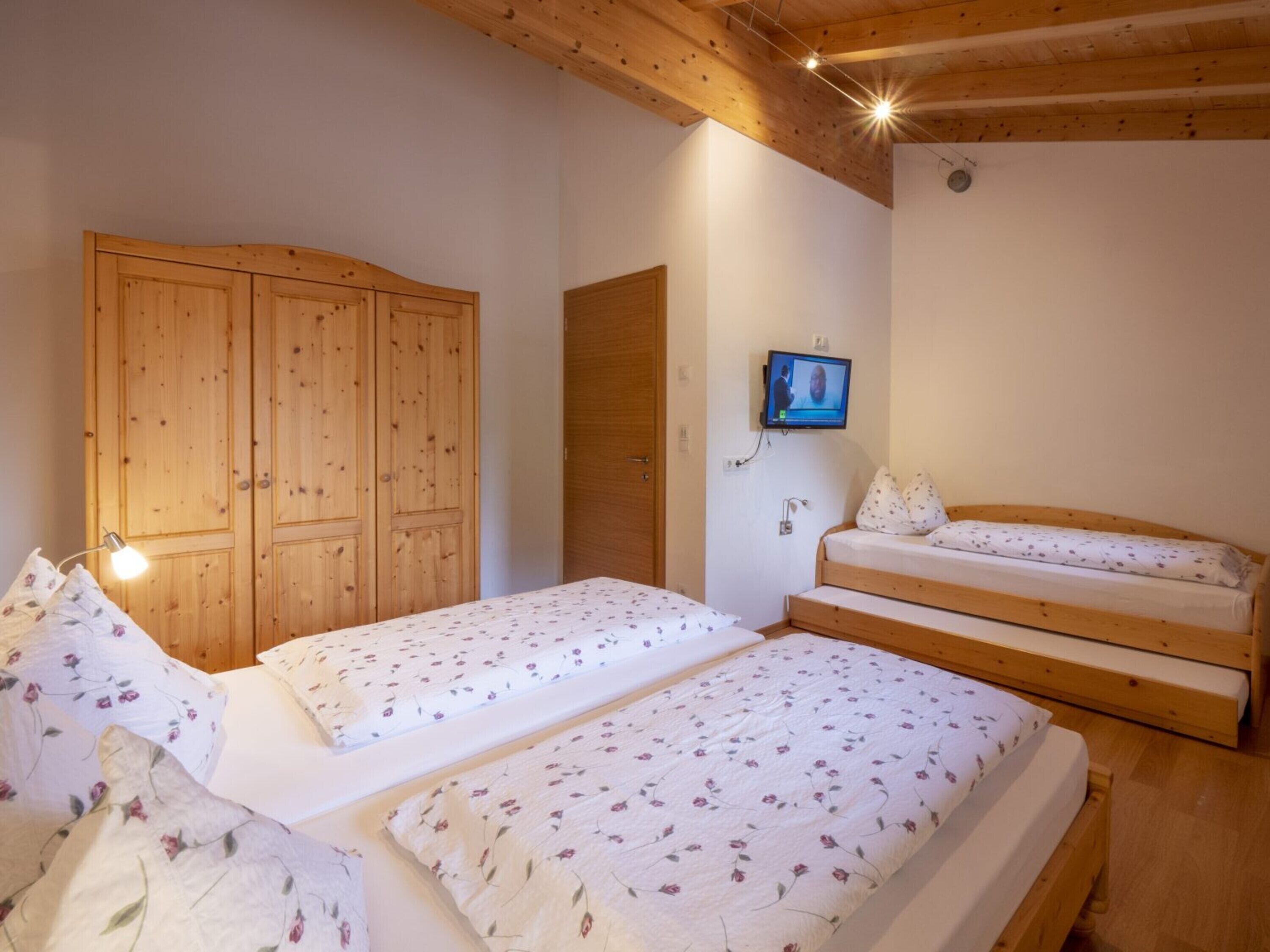 Ein Schlafzimmer mit zwei Betten, einem Holzschrank und einem Fernseher an der Wand.