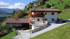 A two-story building with a sloped roof, a gravel driveway, and a car parked in front. - Apartment 'Sultan' with Mountain View, Shared Pool and Wi-Fi (Ratschings - Mareit)