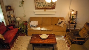 Een woonkamer met een bruine bank, een houten salontafel, een rode fauteuil en een lamp.