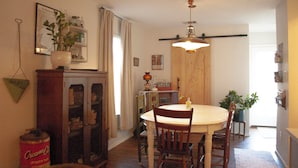 Een eetgedeelte met een ronde tafel, stoelen, een hanglamp, een houten deur en een potplant.