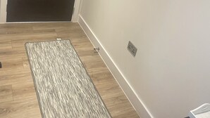 A hallway with a dark door, a wooden floor, and a patterned rug.
