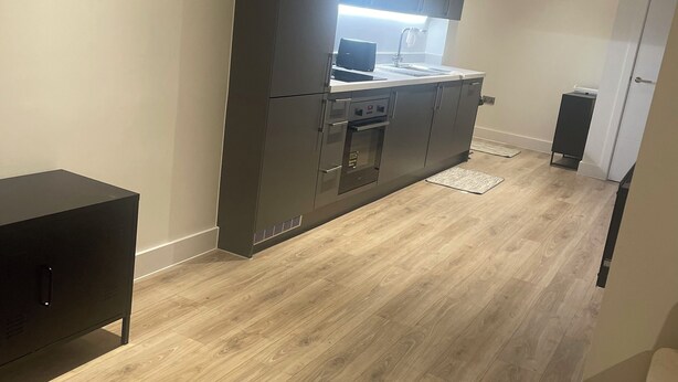 A modern kitchen with built-in appliances, a dining area with a table and chairs, and a wooden floor.