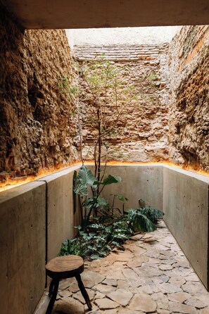 A narrow stone-walled courtyard with a small wooden stool and a plant in the center. - Becino (Oaxaca)