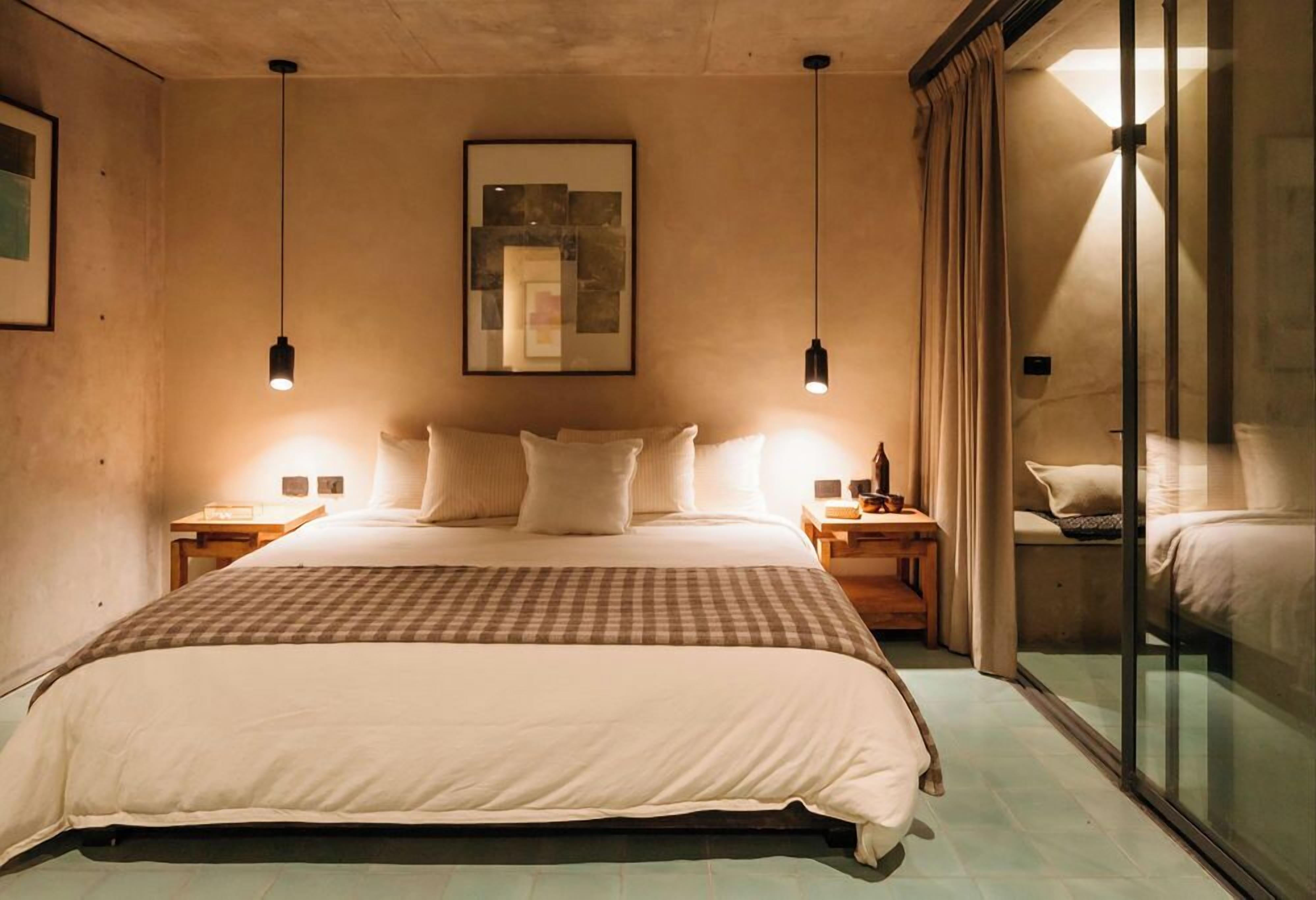 A bedroom with a large bed, two bedside tables, a wall-mounted artwork, and a sliding glass door to a balcony.