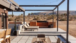 Eine Terrasse im Freien mit Holztisch, Stühlen, einer gepolsterten Sitzecke und einem integrierten Grill.
