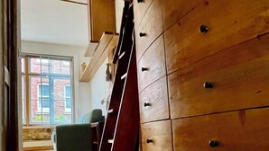 A staircase leading to a wooden staircase railing, a green chair, and a view of a brick building through a window.