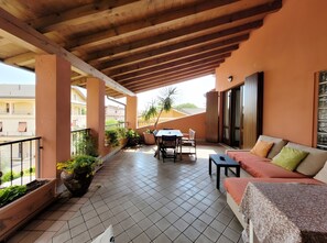 Un balcon abrité, équipé d’une table et de chaises, d’un canapé, de plantes en pot, et offrant une vue sur les bâtiments.