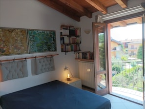 A bedroom with a bed, a bedside table with a lamp, a bookshelf, and a balcony with a view of buildings. - Holiday Home 'Lakeview Dream' with Lake View, Wi-Fi and Air Conditioning (Sirmione)