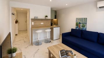 A modern living space with a sofa, a coffee table, and a kitchen area with stools.