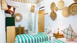 A room with two beds, a wooden wardrobe, a mirror, and woven wall hangings. - RIAD AMR (Tangier)