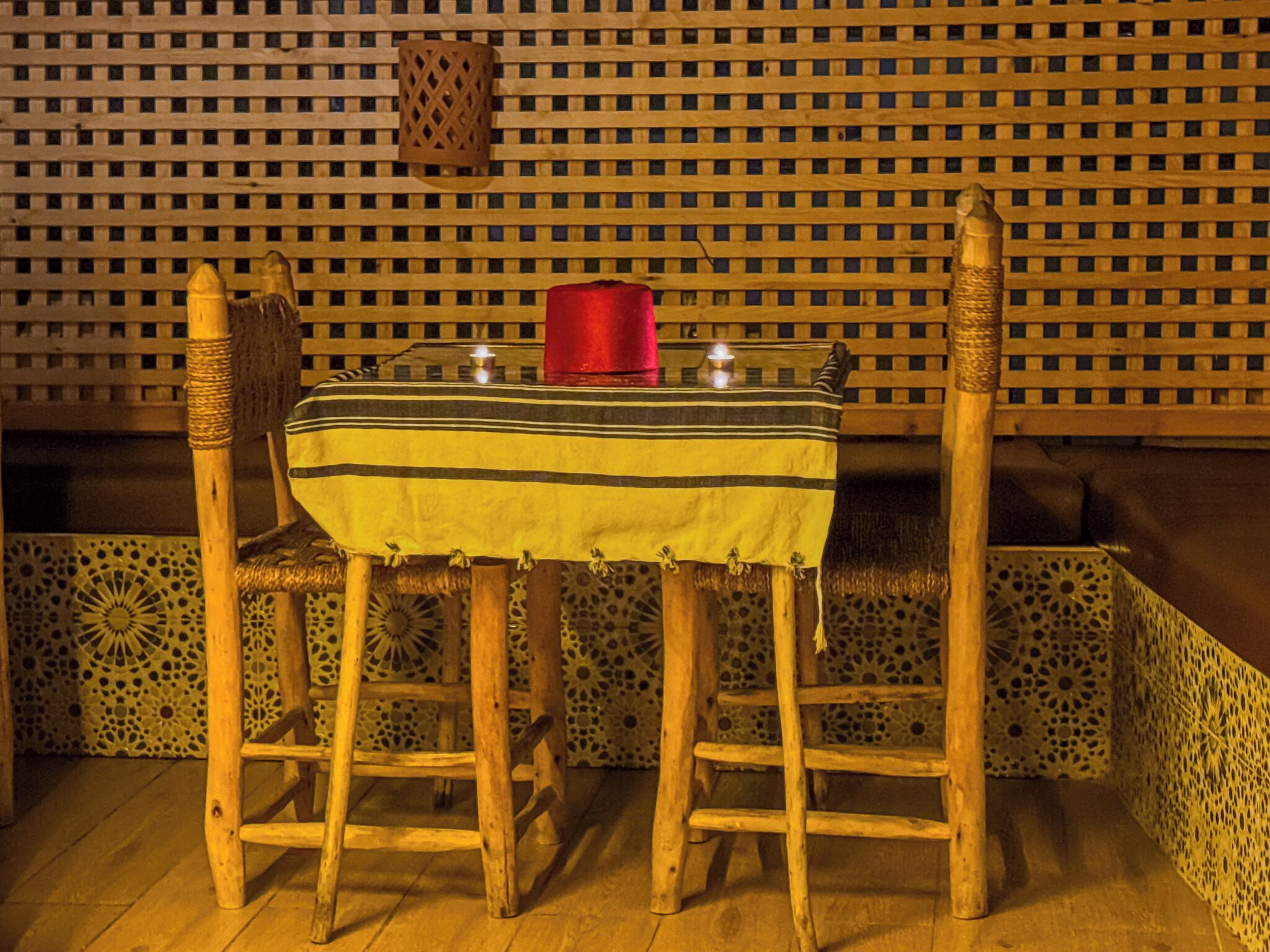 Una mesa de madera con mantel a rayas, dos sillas y una vela roja sobre la mesa.
