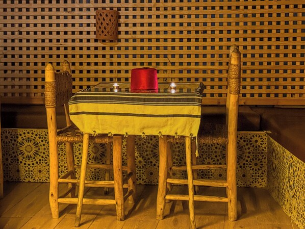 A wooden table with a striped tablecloth, two chairs, and a red candle on the table.