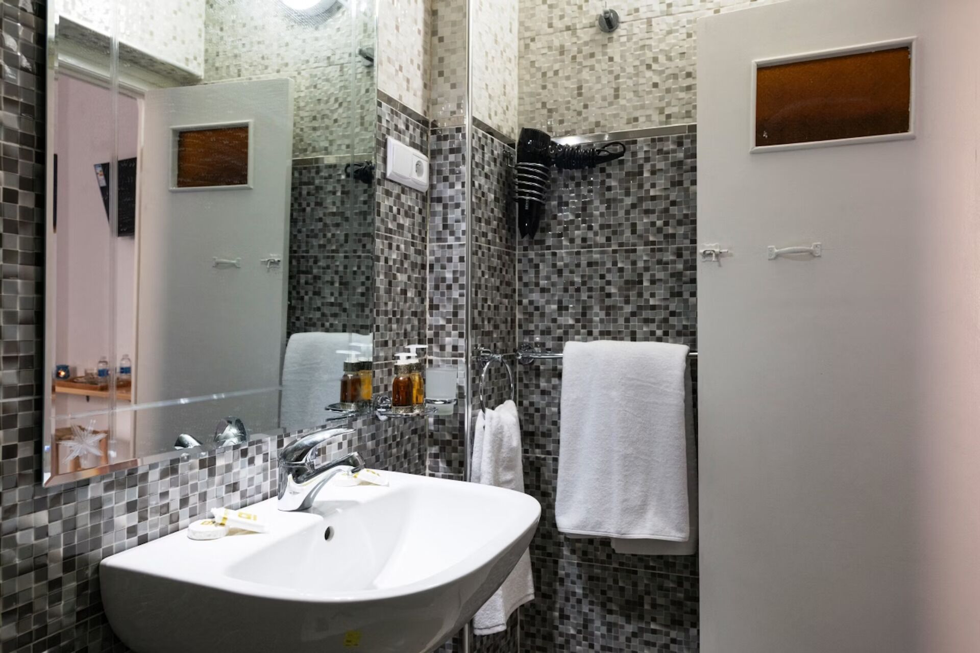 Un baño con lavamanos blanco, espejo y zona de ducha con paredes de azulejos.