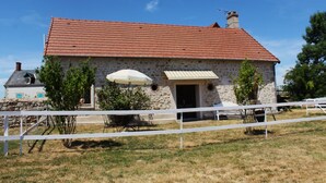 Ein Steinhaus mit rotem Dach, weißem Zaun und einem kleinen Tisch mit Sonnenschirm.