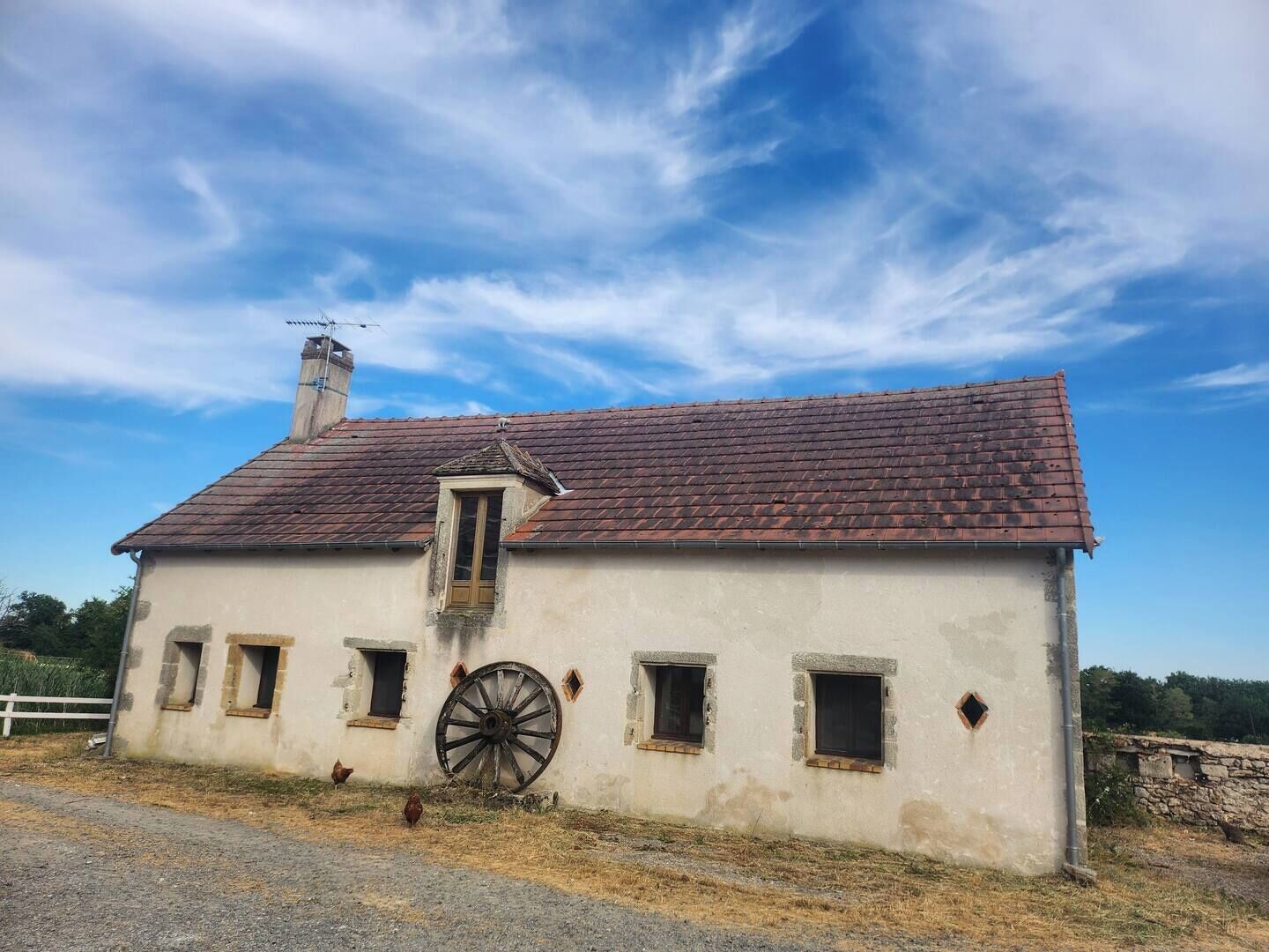 A rustic building with a red-tiled roof, a large wooden wheel, and multiple small windows.