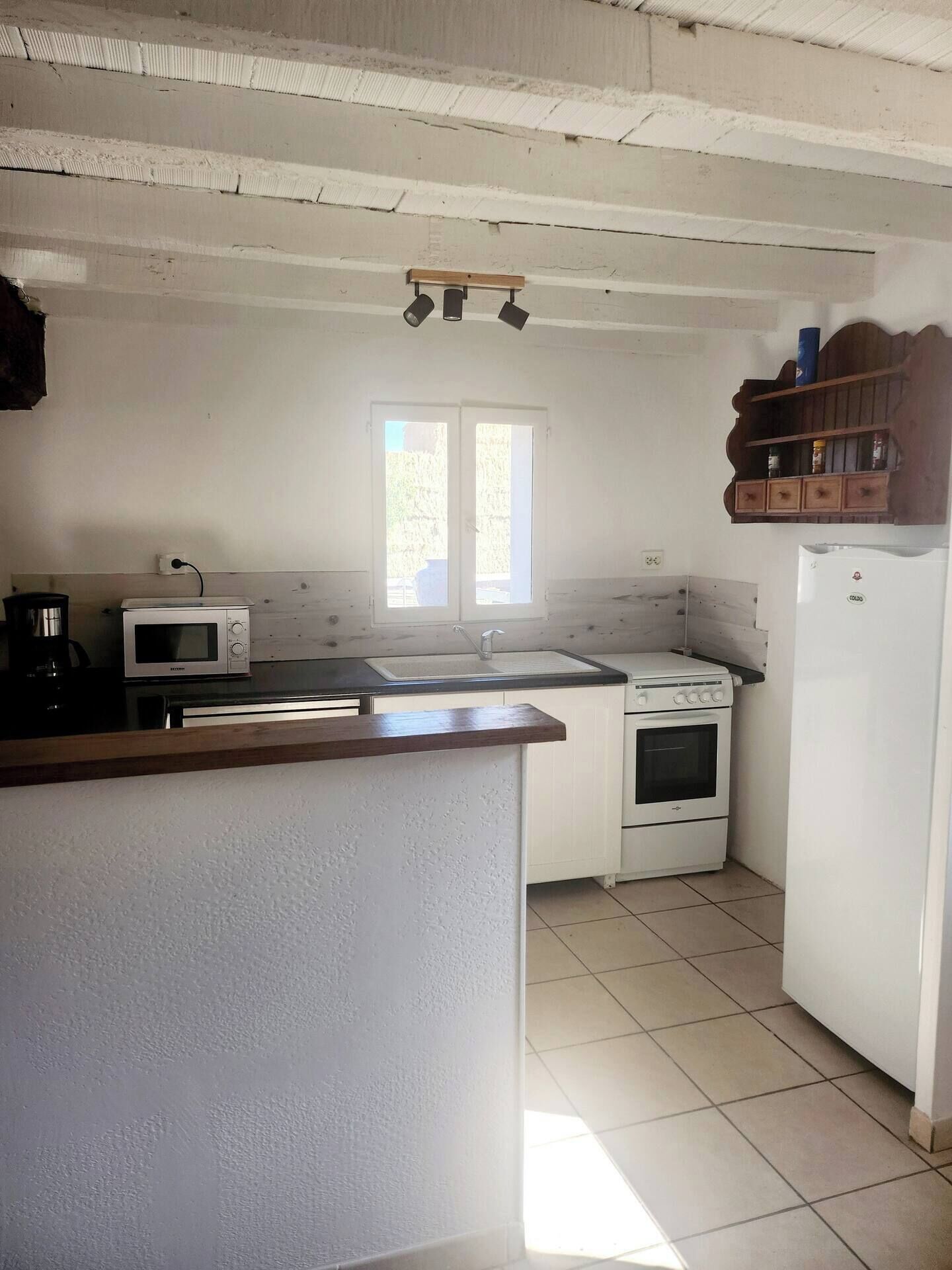 Una cocina con microondas, estufa, pileta y estante de madera.
