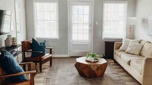 Una sala de estar con una mesa de centro de madera, un sofá color beige y un tapete estampado.