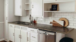Una cocina con armarios blancos, lavavajillas de acero inoxidable y un cubo de basura negro.