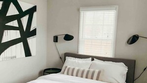 Un dormitorio con una cama, una ventana con persianas y dos lámparas de pared.
