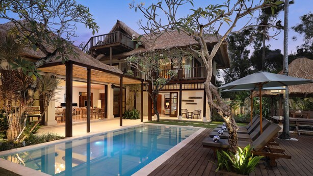A poolside area with a clear pool, lounge chairs, and a thatched-roof building. - Tranquil three bedrooms villa forest view in Jimbaran (Bali)