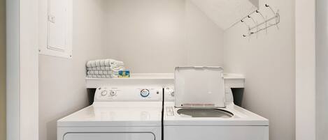 A compact laundry room with a front-loading washer and dryer, a towel rack, and a ceiling light fixture.