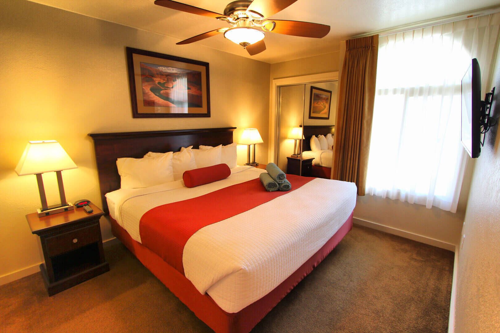A hotel room with a large bed, two bedside tables with lamps, a ceiling fan, and a window with curtains.