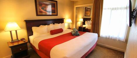 A hotel room with a large bed, two bedside tables with lamps, a ceiling fan, and a window with curtains.