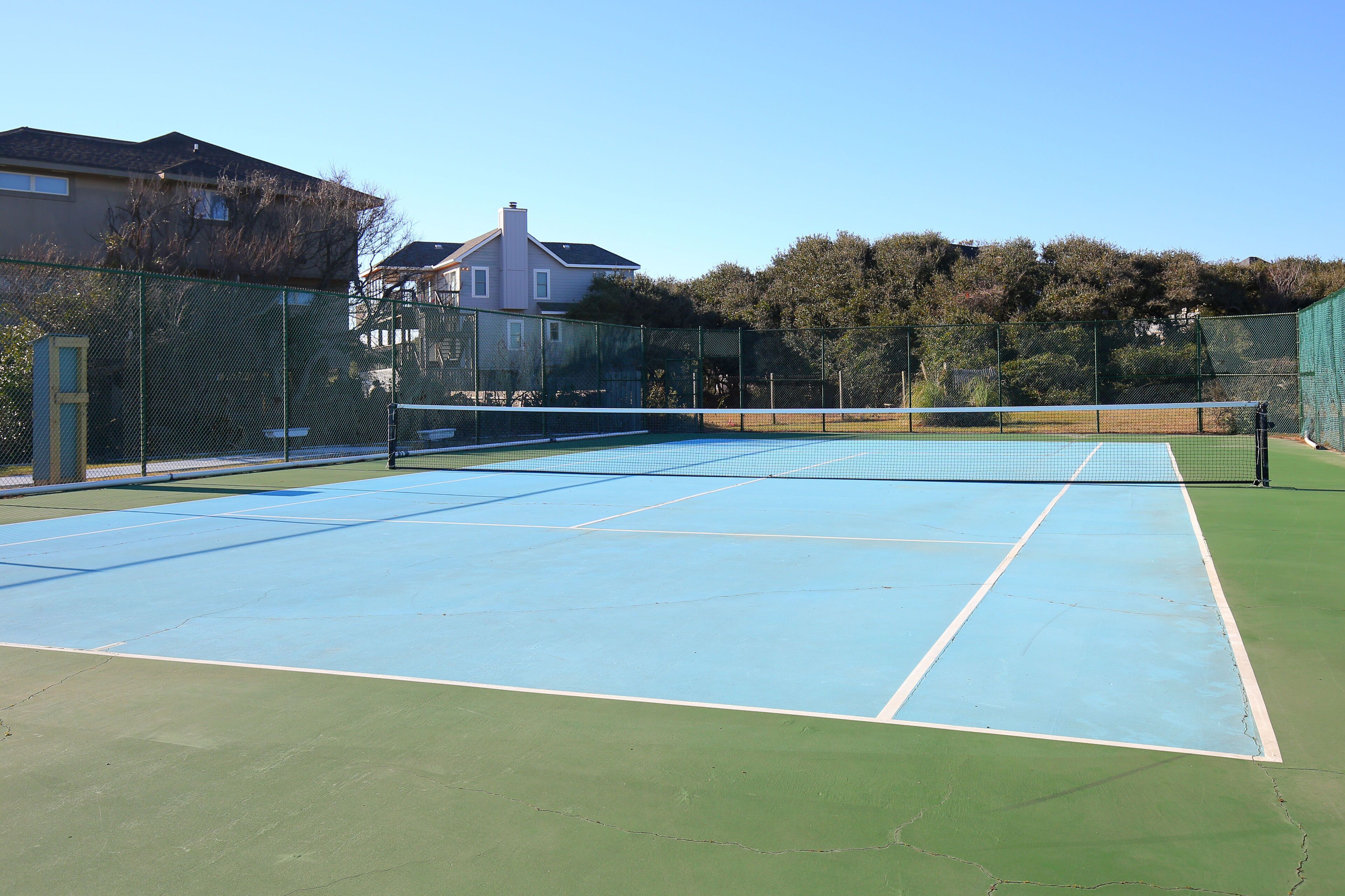 A tennis court with a net, surrounded by a green fence and trees.