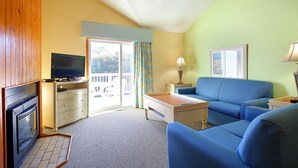 A room with a fireplace, a television, a sofa, a table, and a window with curtains. - 2BR Condo w/ Indoor Pool + Beach Access (Duck)