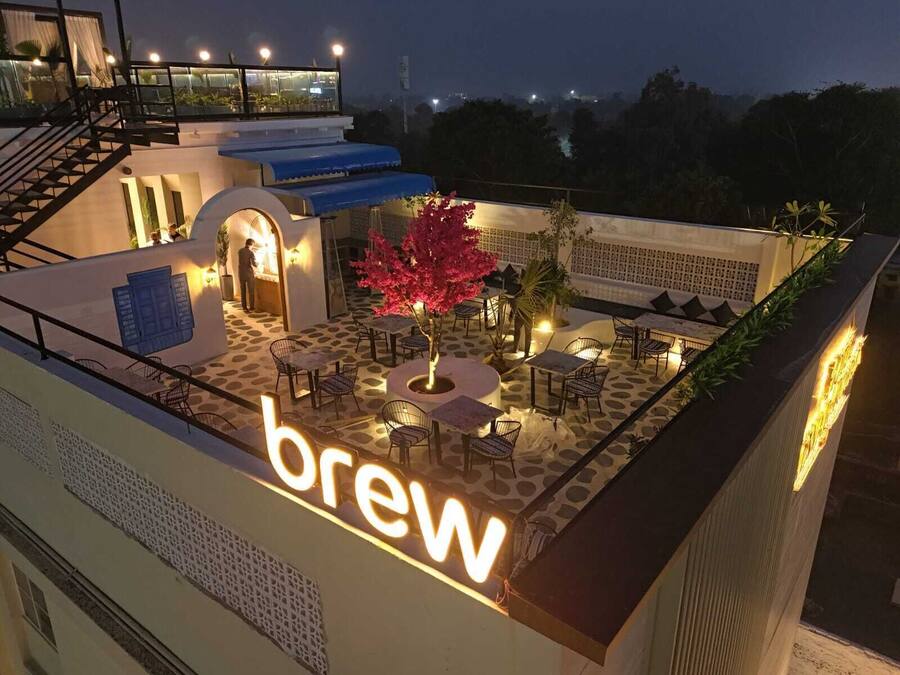 An outdoor seating area with tables and chairs, a tree, and a sign that reads "brew".