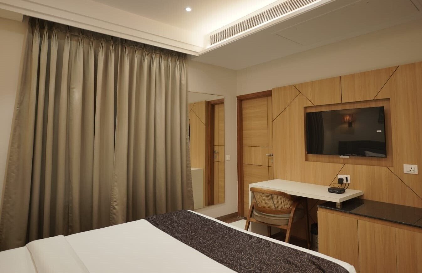 Une chambre d’hôtel équipée d’un lit, d’un bureau, d’une chaise, d’une télévision et d’une grande fenêtre avec des rideaux.