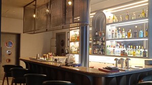 Een bar met een toonbank, krukken en een goed gevulde plank met drankflessen.