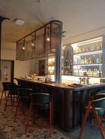 Zona de bar con mostrador, taburetes y una estantería repleta de licores.