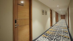 Een hotelgangen met houten deuren, kamer 210 met nummer, en een vloer met patroon.