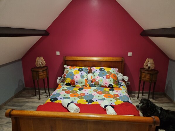 A bedroom with a wooden bed, colorful floral bedding, and a red accent wall.