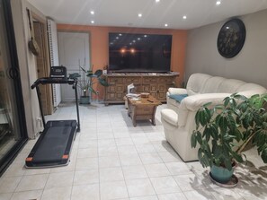 A living room with a treadmill, a couch, a wooden cabinet, and a large window.